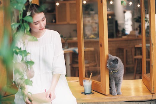 pexels-photo-28263793-28263793 A serene moment in a cozy cafe featuring a woman enjoying leisure time with a cat.
